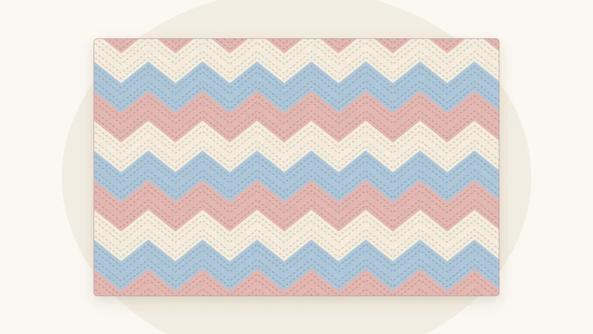 A chevron ripple crochet baby blanket with zigzag stripes in dusty rose, cream and pale blue, lying flat