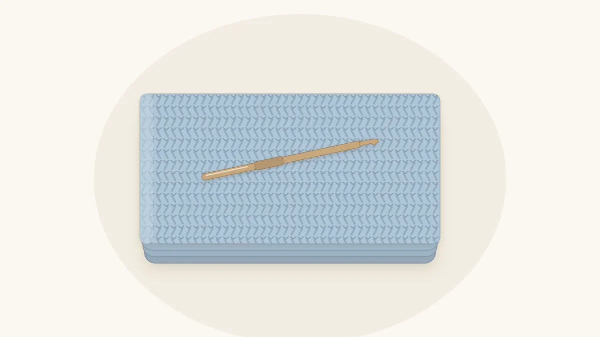 A pale blue half double crochet baby blanket folded in thirds with a crochet hook resting on top