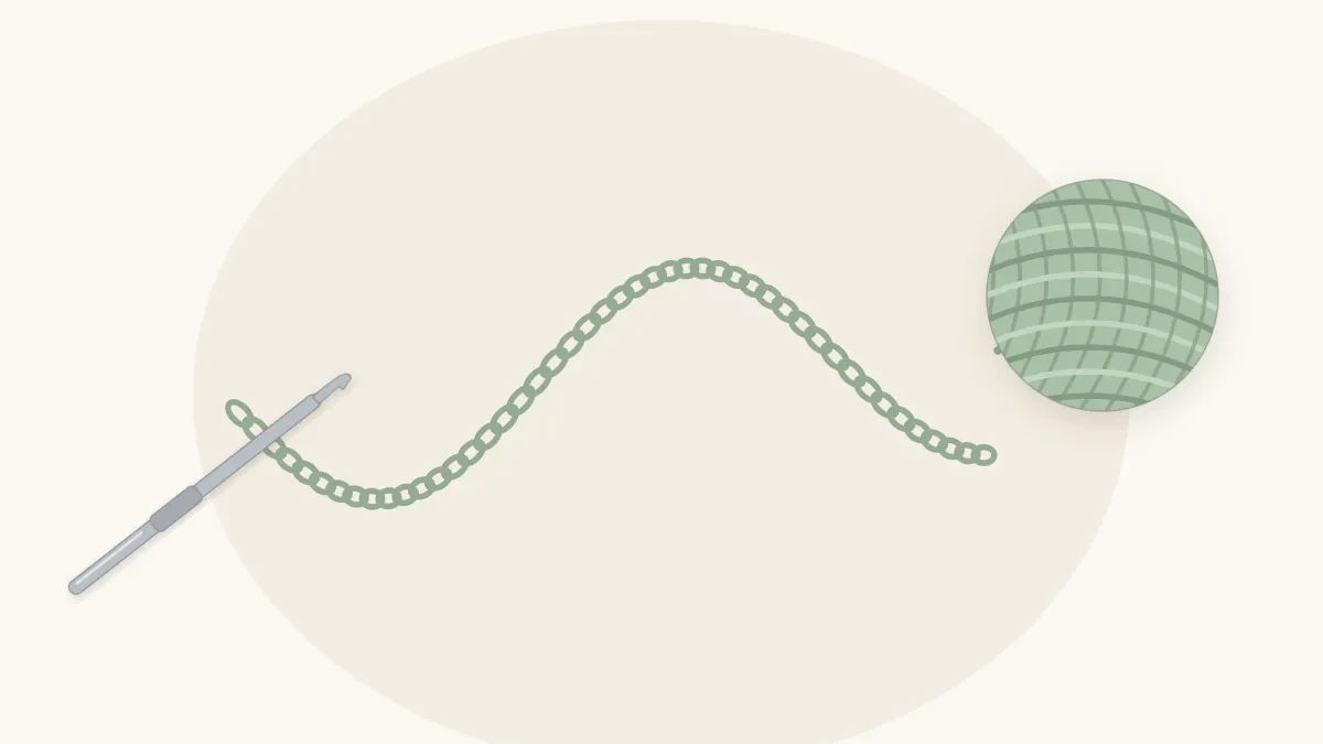 A long crochet foundation chain in sage green curving across a cream surface with a hook at one end and a yarn ball at the other