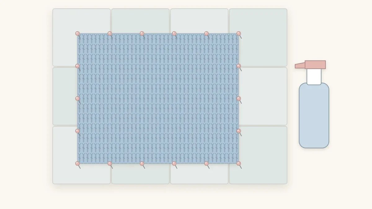A pale blue crochet baby blanket pinned flat and square on interlocking blocking mats with a spray bottle beside it