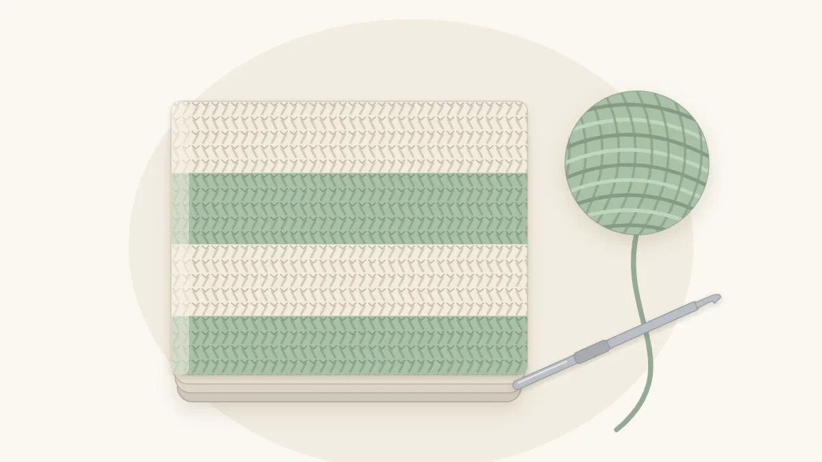 Folded cream and sage green crocheted baby blanket lying flat with a ball of sage yarn and a crochet hook beside it