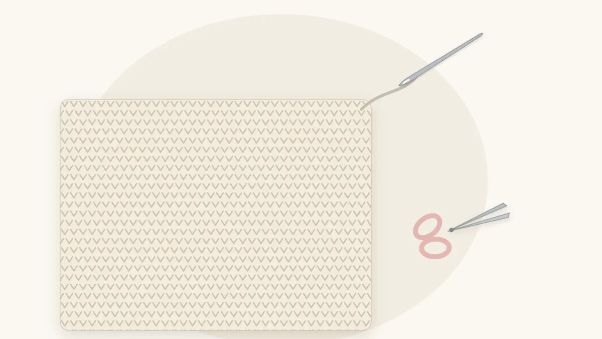 The corner of a cream crochet blanket with a blunt yarn needle threaded with a yarn tail, and small scissors nearby