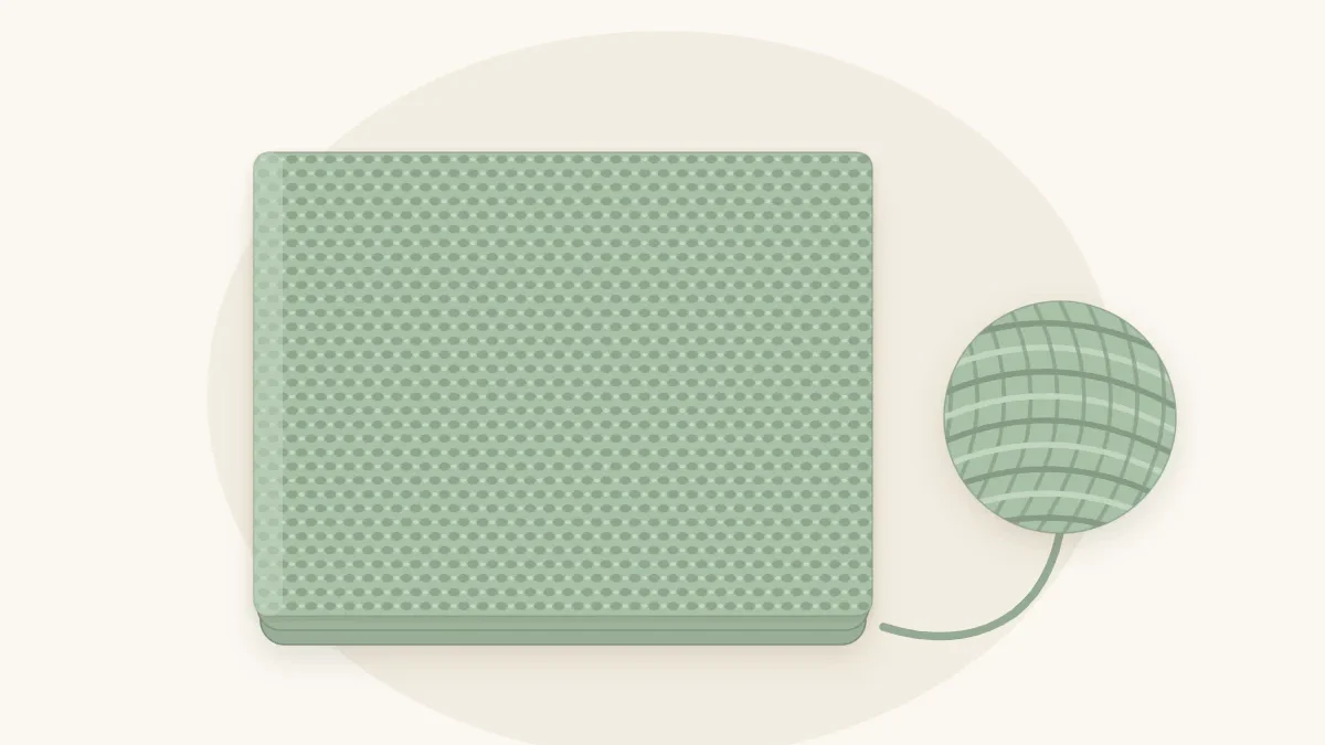 A moss stitch baby blanket in soft sage with a fine woven-looking texture, folded once, with a sage yarn ball