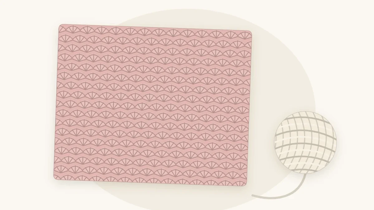 A shell stitch crochet baby blanket in dusty rose with rows of fan-shaped stitches, lying flat with a cream yarn ball