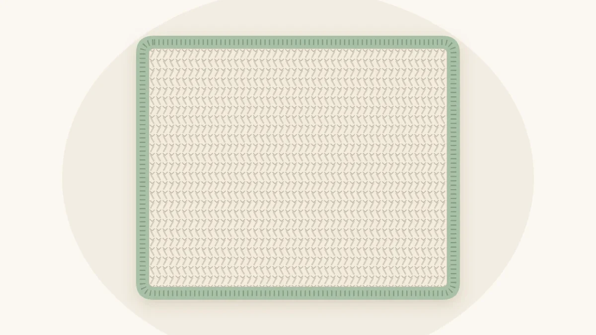 A cream crochet baby blanket with a neat contrasting sage green border around all four edges, shown from above