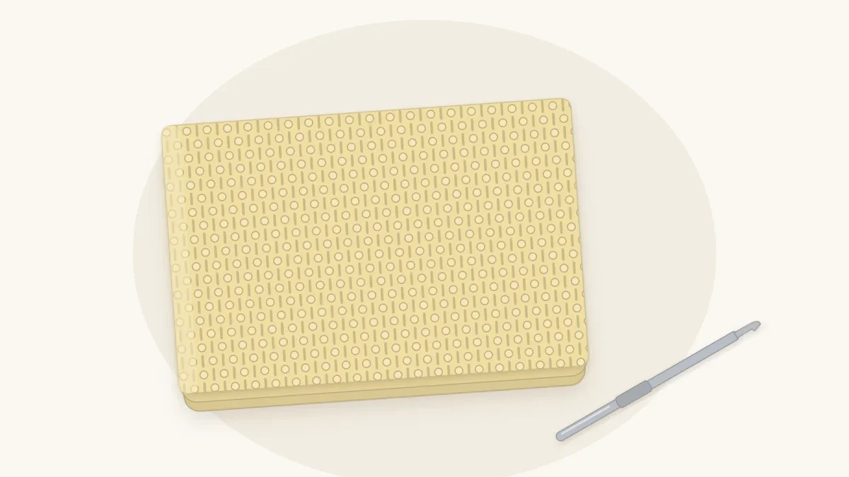 A textured crochet baby blanket in butter yellow with a pebbly bumpy surface, loosely folded, with a crochet hook